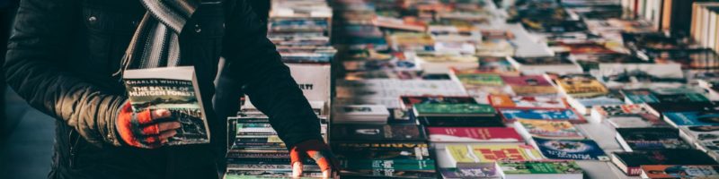 person holding book while browsing on book lot